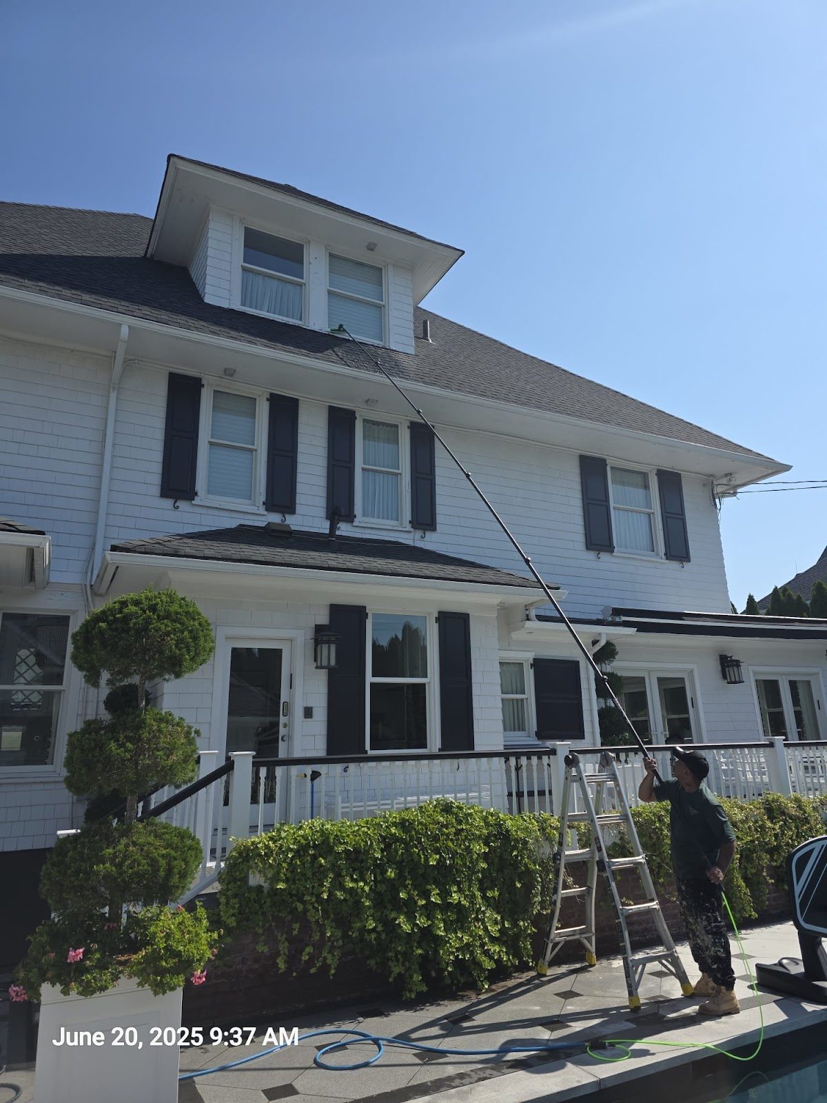 A BusyBees technician cleaning second floor windows with a water fed pole on a house in Brooklyn